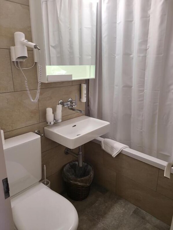A bathroom with a toilet, sink, and shower curtain. - Residence Hotel & Apartments (Grindelwald)