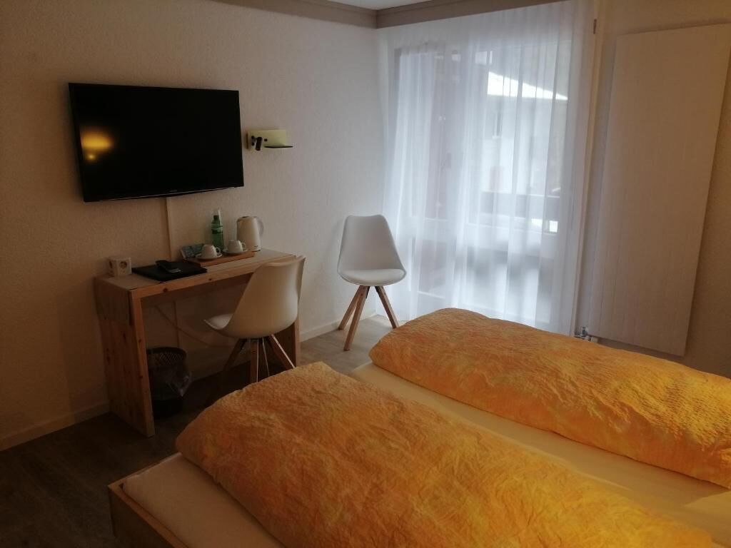 Una camera d'albergo con un letto, una scrivania con una sedia, una televisione e una finestra con tende.