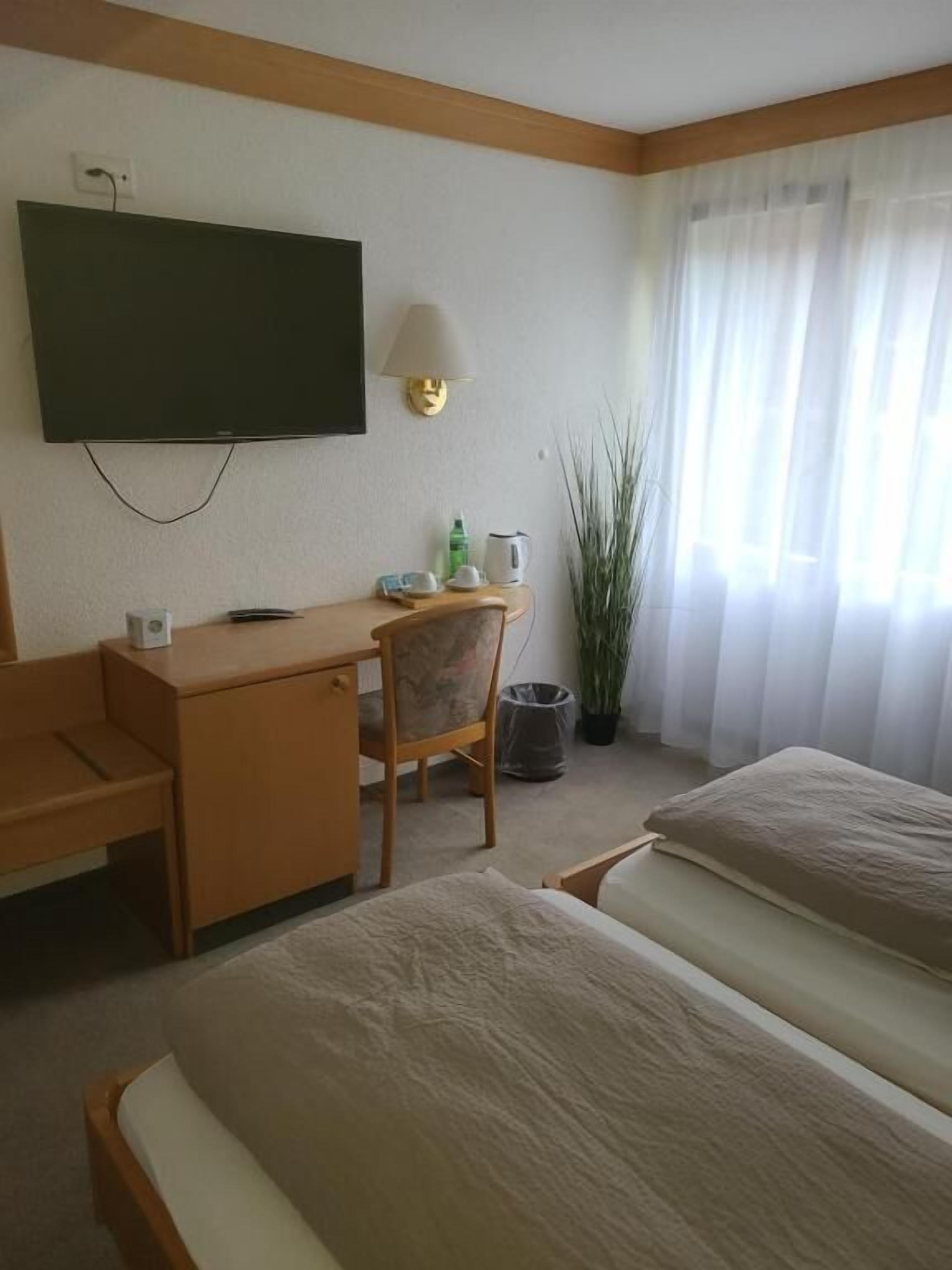 Habitación de hotel con cama, escritorio, silla, televisión instalada en la pared y ventana con cortinas.