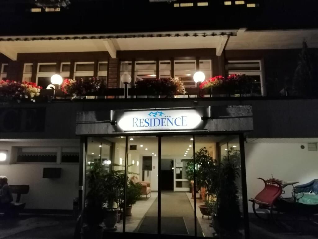 A hotel entrance with a sign reading 'RESIDENCE' and a covered outdoor seating area with potted plants.