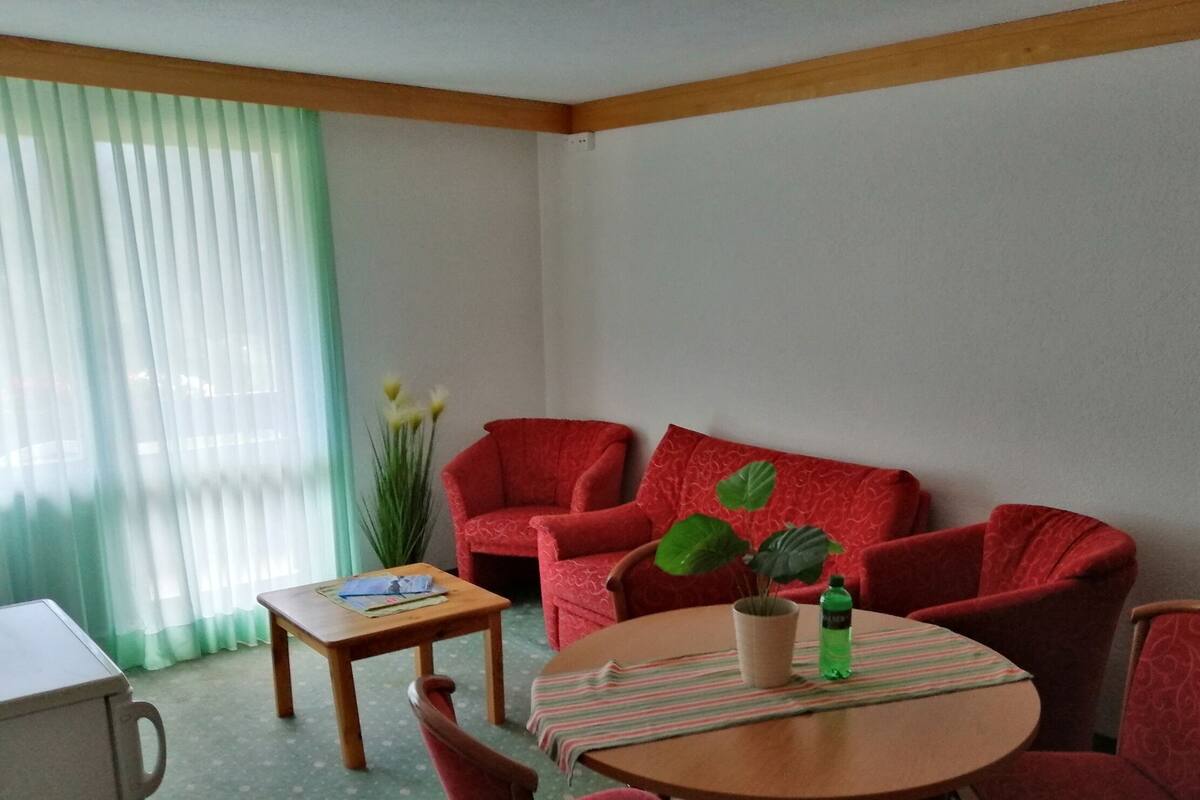 Quarto com sofá vermelho, uma mesa de madeira pequena, uma planta em vaso e toalha de mesa listrada.
