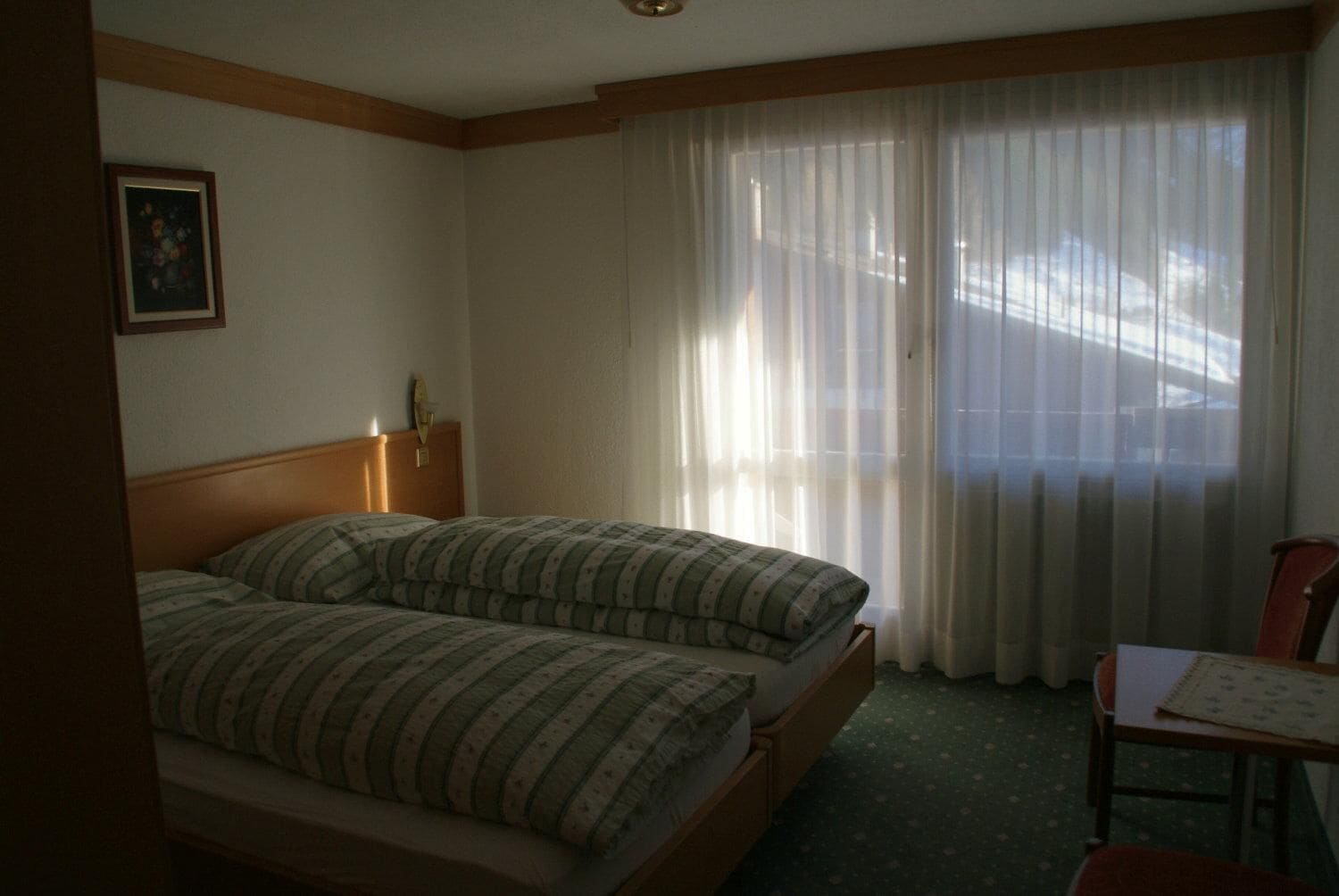 Una camera d'albergo con un letto, una sedia, un tavolo e una finestra con tende.