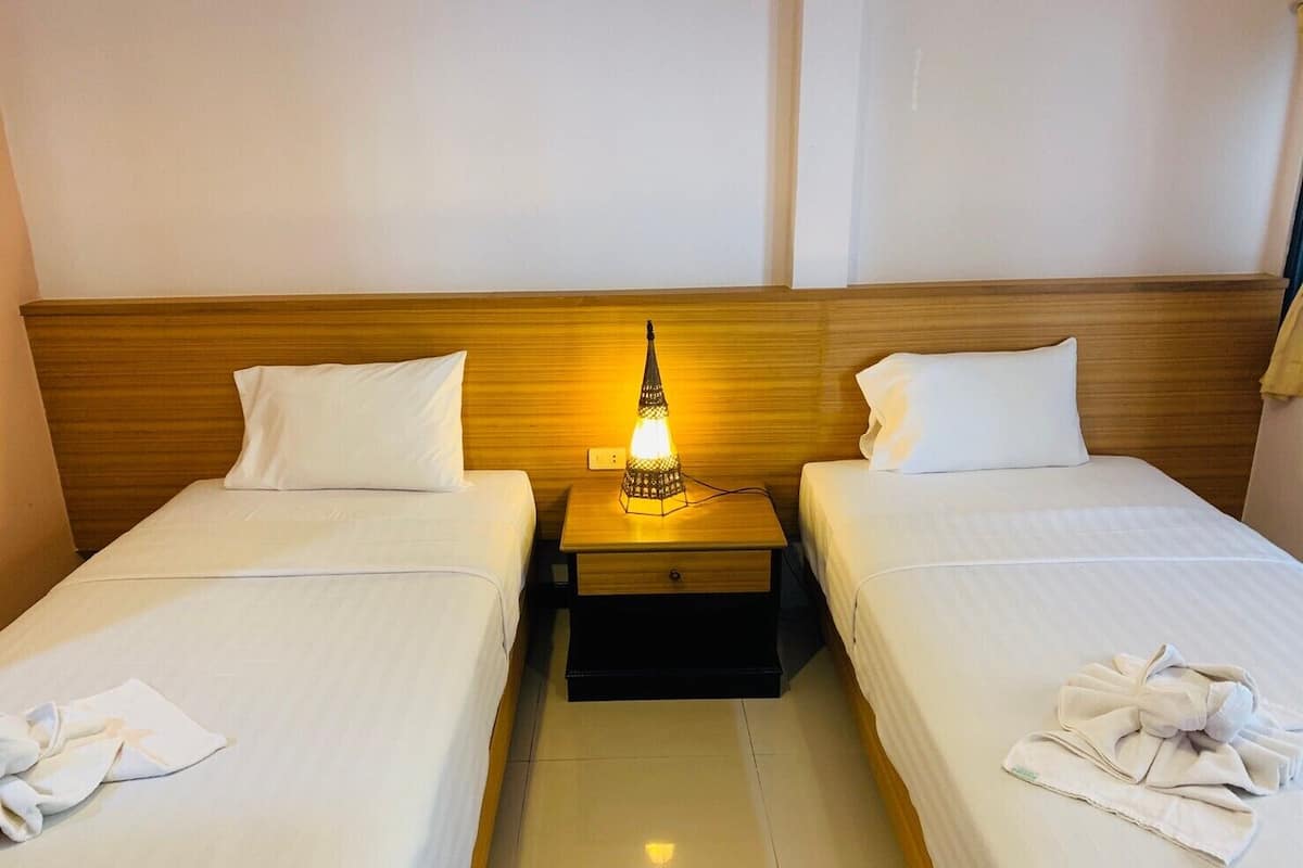 A hotel room with two single beds, a nightstand with a lamp, and towels on each bed.