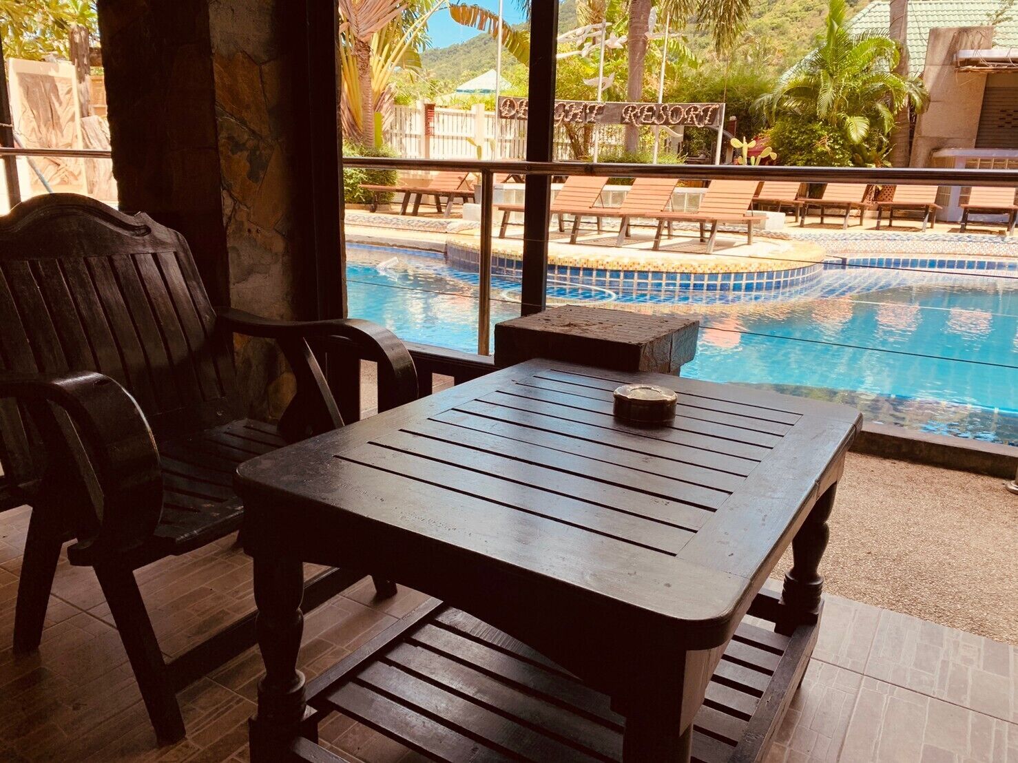 A wooden table and chairs near a pool with a sign reading "HOTEL RESORT".