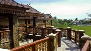 Un bâtiment traditionnel en bois, doté de balustrades finement ouvragées et d’un chemin de pierre menant à un paysage verdoyant et luxuriant.