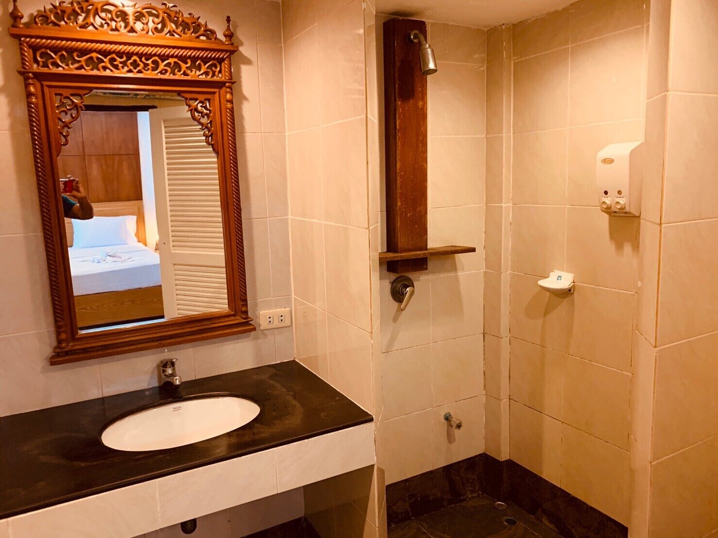 A bathroom with a wooden-framed mirror, a white sink, a shower, and a toilet.
