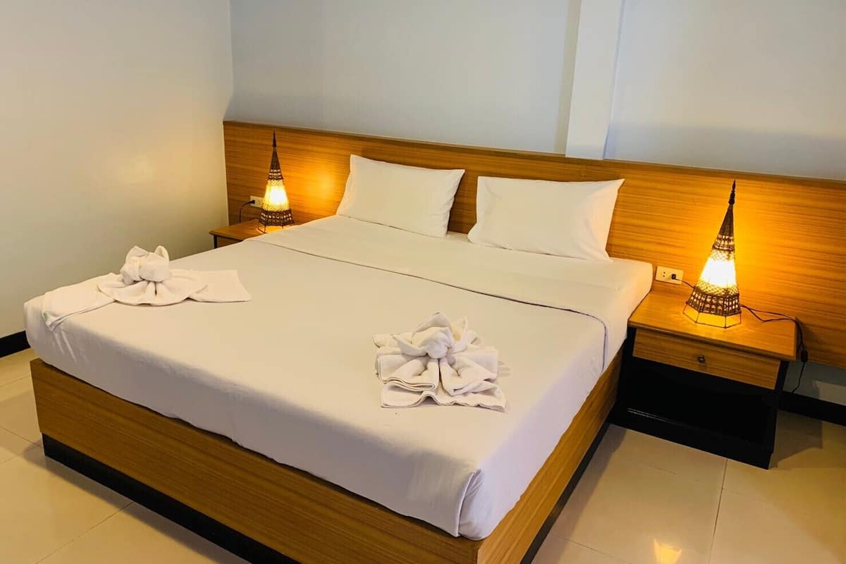 A neatly made bed with white linens and towels, two bedside lamps, and a wooden headboard.
