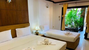 Une chambre d’hôtel avec deux lits, chacun étant muni d’une serviette. On y trouve une table de chevet avec une lampe, une fenêtre avec des rideaux et une vue sur la verdure environnante.