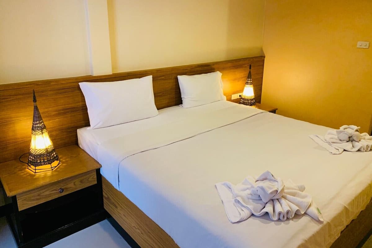 A neatly made bed with white linens, two bedside lamps, and a pile of towels on the bed.