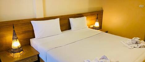 Una cama bien hecha con sábanas blancas, dos lámparas de noche y una pila de toallas sobre la cama.