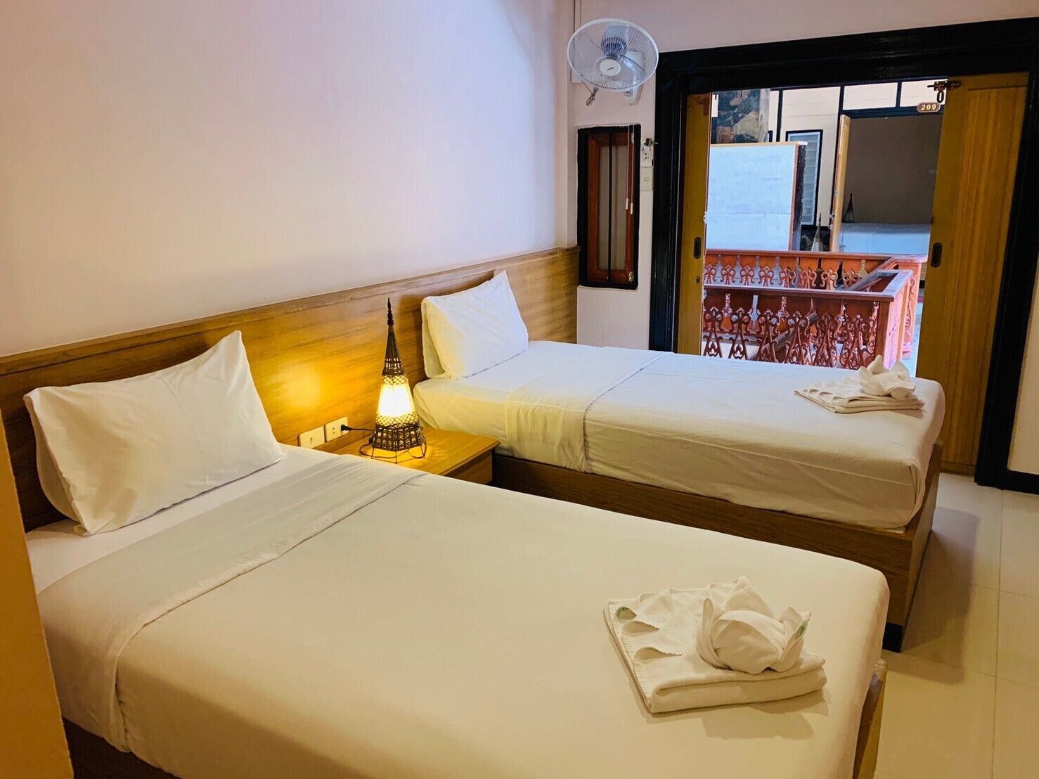 Une chambre d’hôtel avec deux lits, une table de chevet avec une lampe et un balcon avec une balustrade.