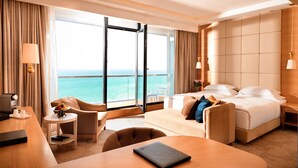 A modern hotel room with a large balcony, a sofa, a desk, and a bed.