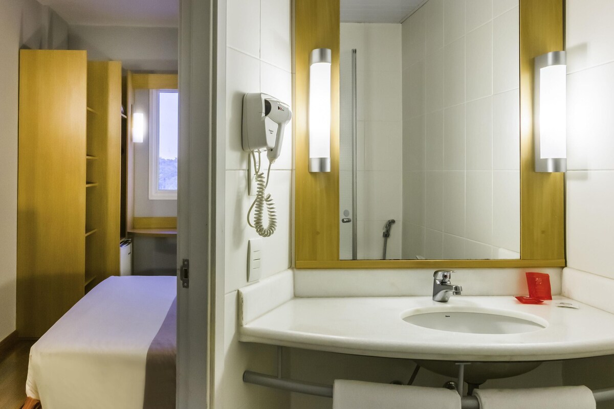 A hotel bathroom with a white sink, a mirror, a hairdryer, and a shower.