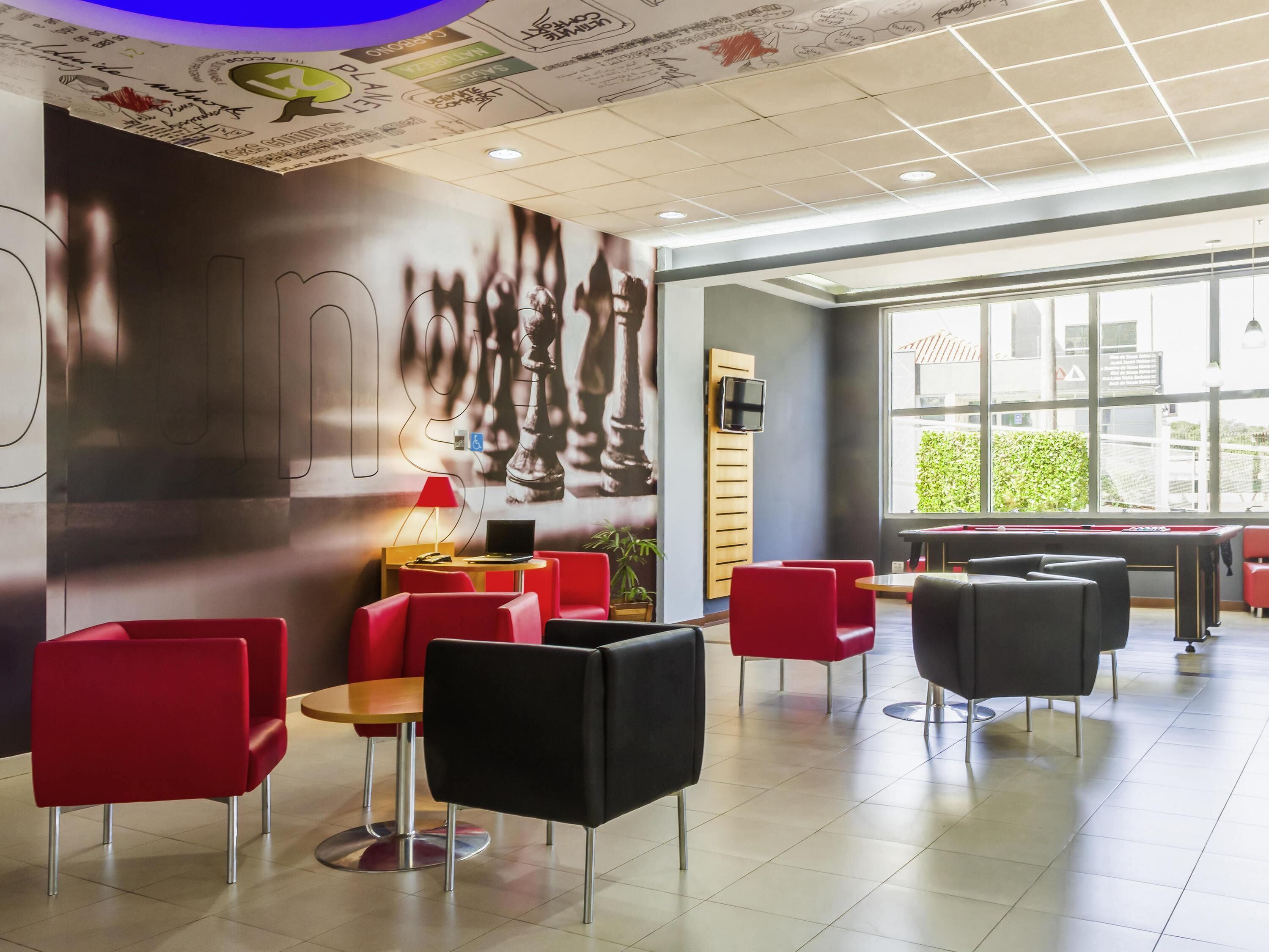 A modern indoor space with red and black chairs, a pool table, and a large window providing natural light.