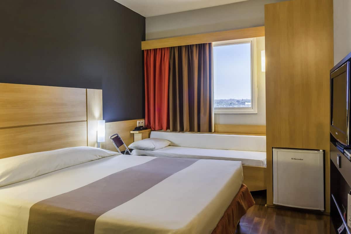Une chambre d’hôtel avec deux lits, une télévision, un mini-réfrigérateur et une fenêtre avec des rideaux.