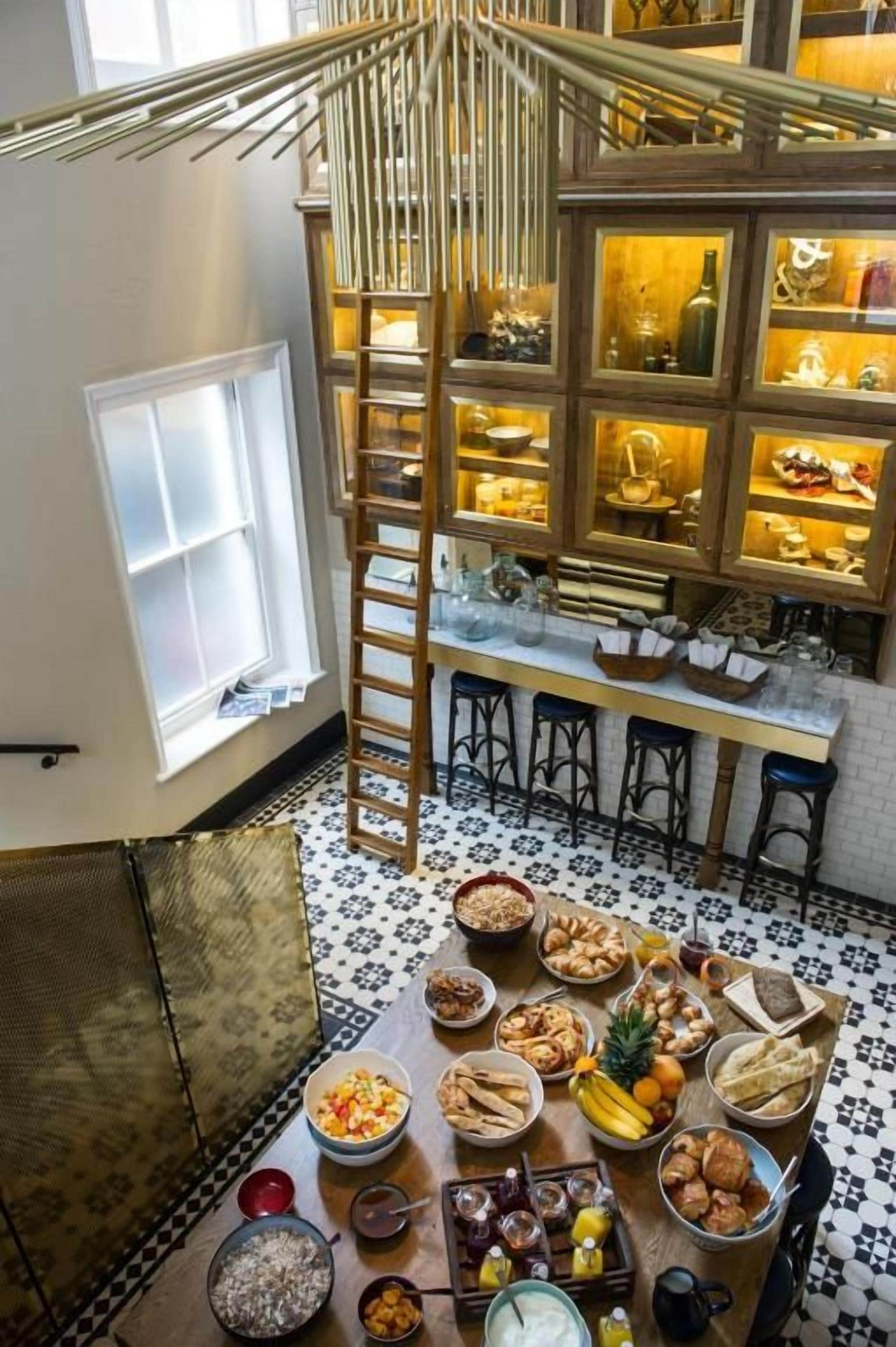 A dining area with a high ceiling, a central table with food, and a staircase leading to upper levels.