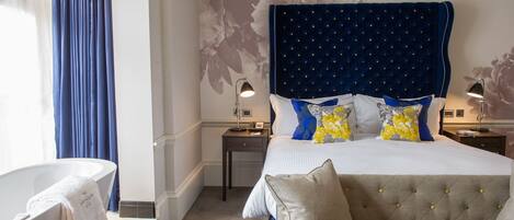 A bedroom with a large bed, a sofa, a bathtub, and a nightstand with a lamp.