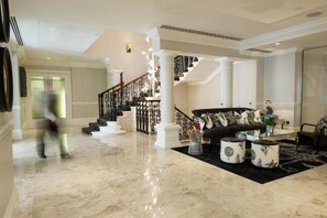 A spacious lobby with a marble floor, a black sofa with patterned cushions, a staircase with ornate railings, and a glass partition wall. - The Ampersand Hotel - Small Luxury Hotels of the World (London)