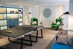 A room with a ping pong table, two green armchairs, a blue sofa, and a bookshelf with various items. - The Ampersand Hotel - Small Luxury Hotels of the World (London)