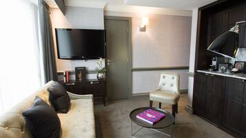 A modern living room with a sofa, a coffee table, a television, and a kitchen area with a coffee machine.