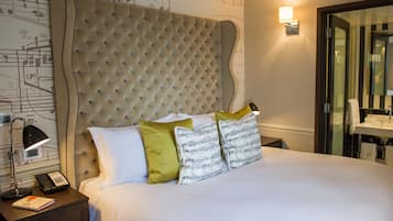Une chambre d’hôtel avec une tête de lit capitonnée, une lampe de chevet, un téléphone et un lit recouvert de draps blancs et agrémenté d’oreillers à motifs.