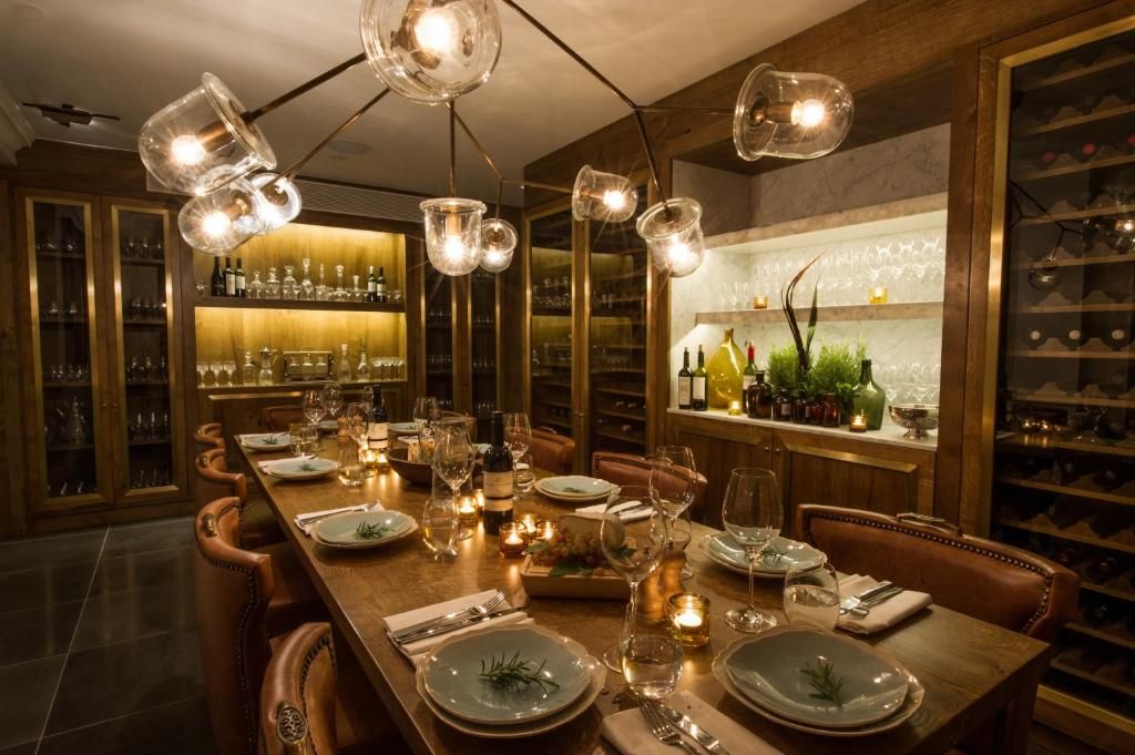 Uma sala de jantar com uma mesa comprida posta para uma refeição, rodeada por cadeiras, com um espaço de bar ao fundo.