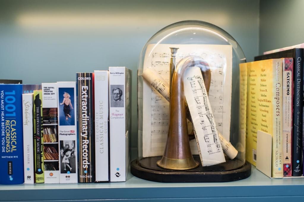 A bookshelf with various books and a brass bell on a stand.