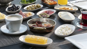 A breakfast table with various dishes, a cup of coffee, and a glass of orange juice, set on a balcony overlooking a cityscape.