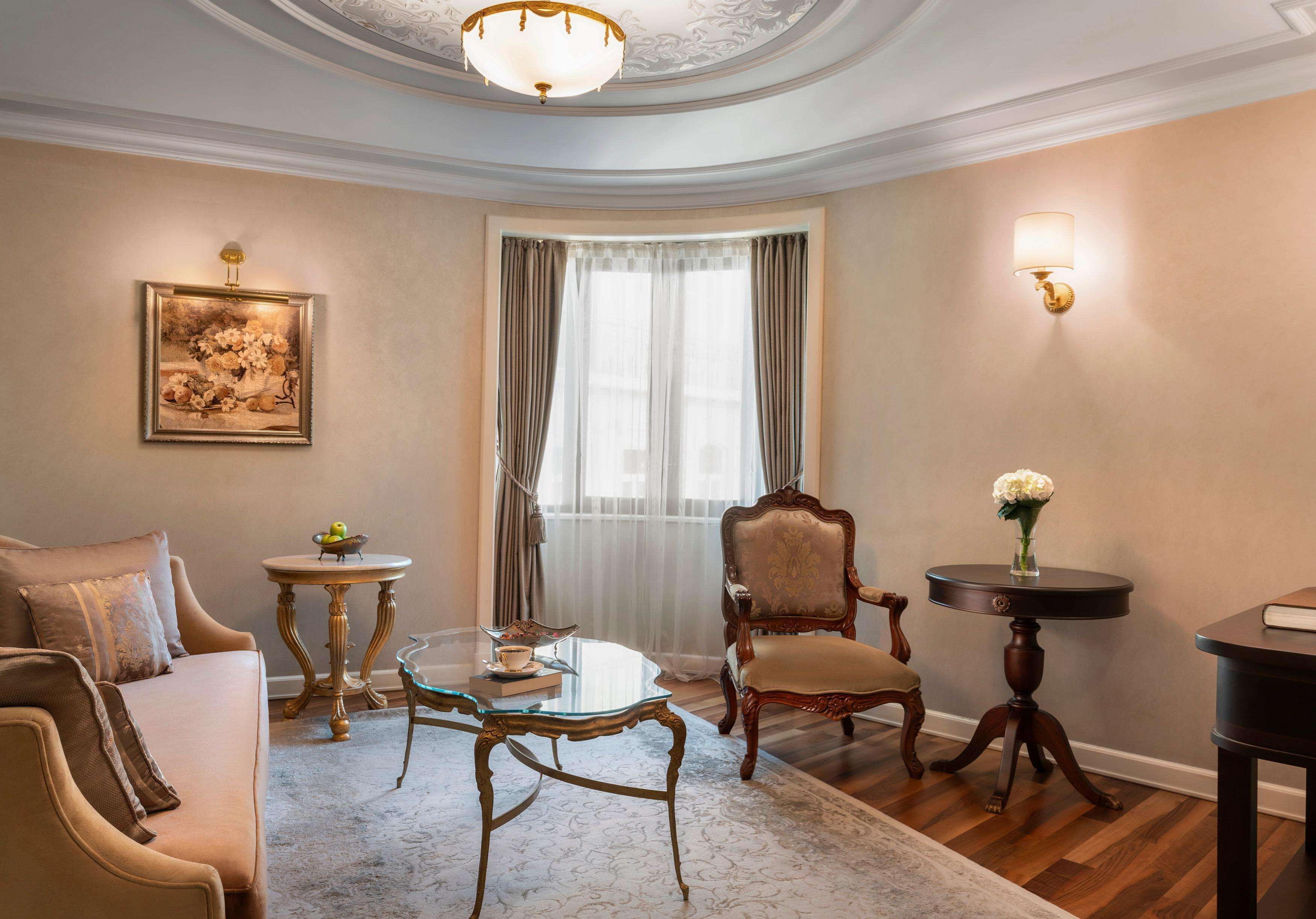 A well-appointed living room with a sofa, a glass coffee table, a wooden chair, a round table, and a chandelier.