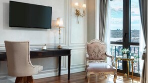 A room with a flat-screen TV, a desk with a lamp, a chair, and a view of a cityscape through large windows. - Rixos Pera Istanbul - Nickelodeon Play Access (Istanbul)