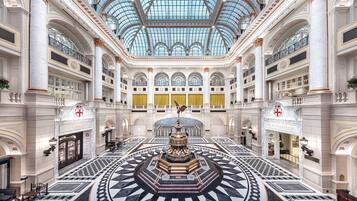 A grand hotel lobby with a central fountain, high ceilings, and intricate marble flooring.