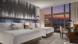 A modern hotel room with a large bed, two bedside tables, a desk, and a view of a cityscape at dusk. - Conrad Macao (Cotai)