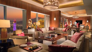 A modern hotel room with a large window offering a city view, a cozy seating area with a sofa and armchairs, a wooden coffee table, and a chandelier. - Conrad Macao (Cotai)