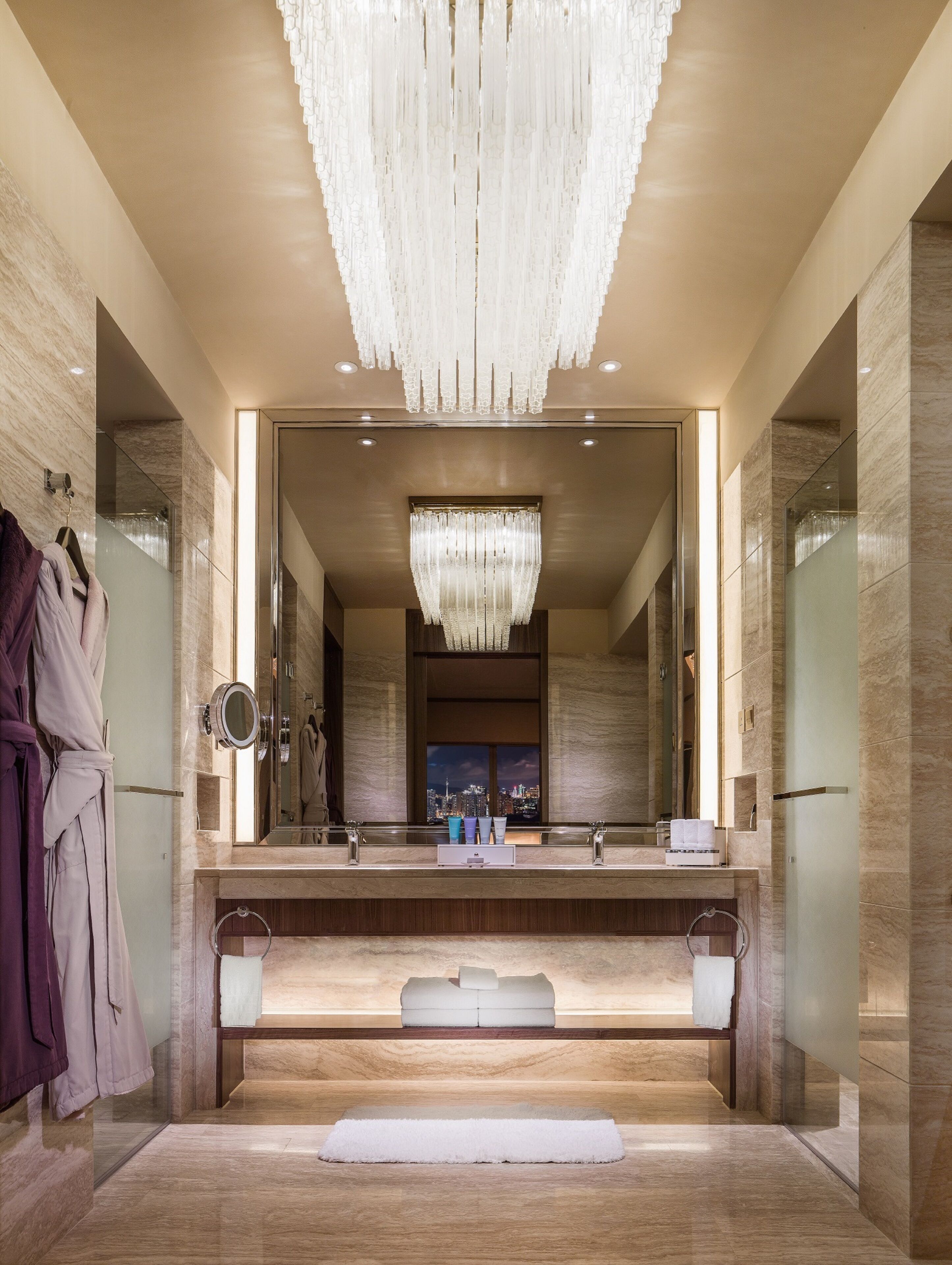 A luxurious bathroom with a large mirror, a chandelier, and a view of the cityscape.