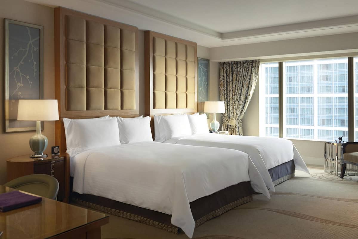 Una habitación de hotel con una cama grande, un escritorio, una silla, una lámpara, una mesita de noche y una ventana con cortinas.