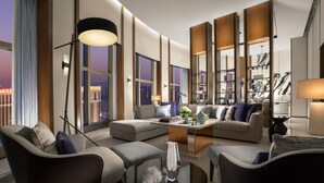 A modern living room with a sofa, armchairs, and a coffee table. There are large windows with a city view, a bookshelf, and a lamp. - Conrad Macao (Cotai)
