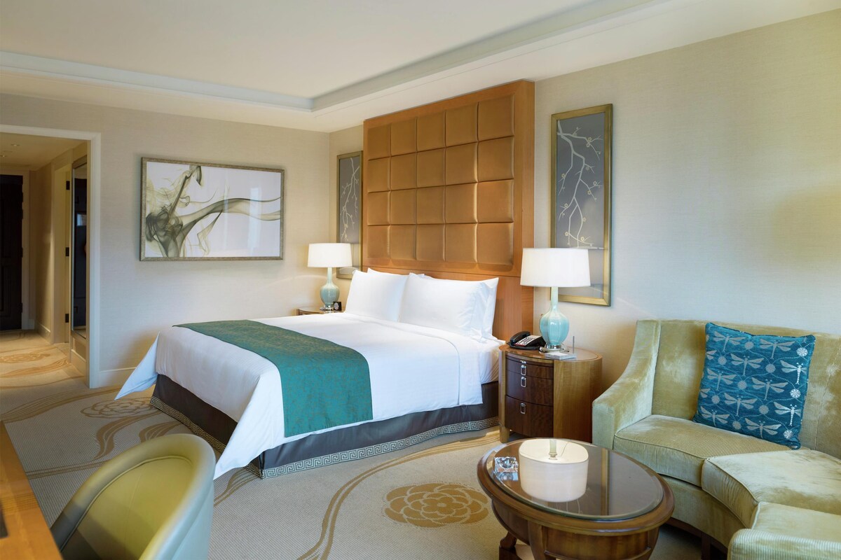 A hotel room with a large bed, two bedside tables, a sofa, a chair, and a small table.