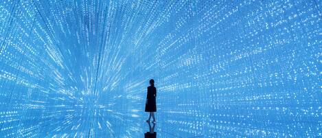 A person standing in front of a large, illuminated blue structure with a radial pattern.