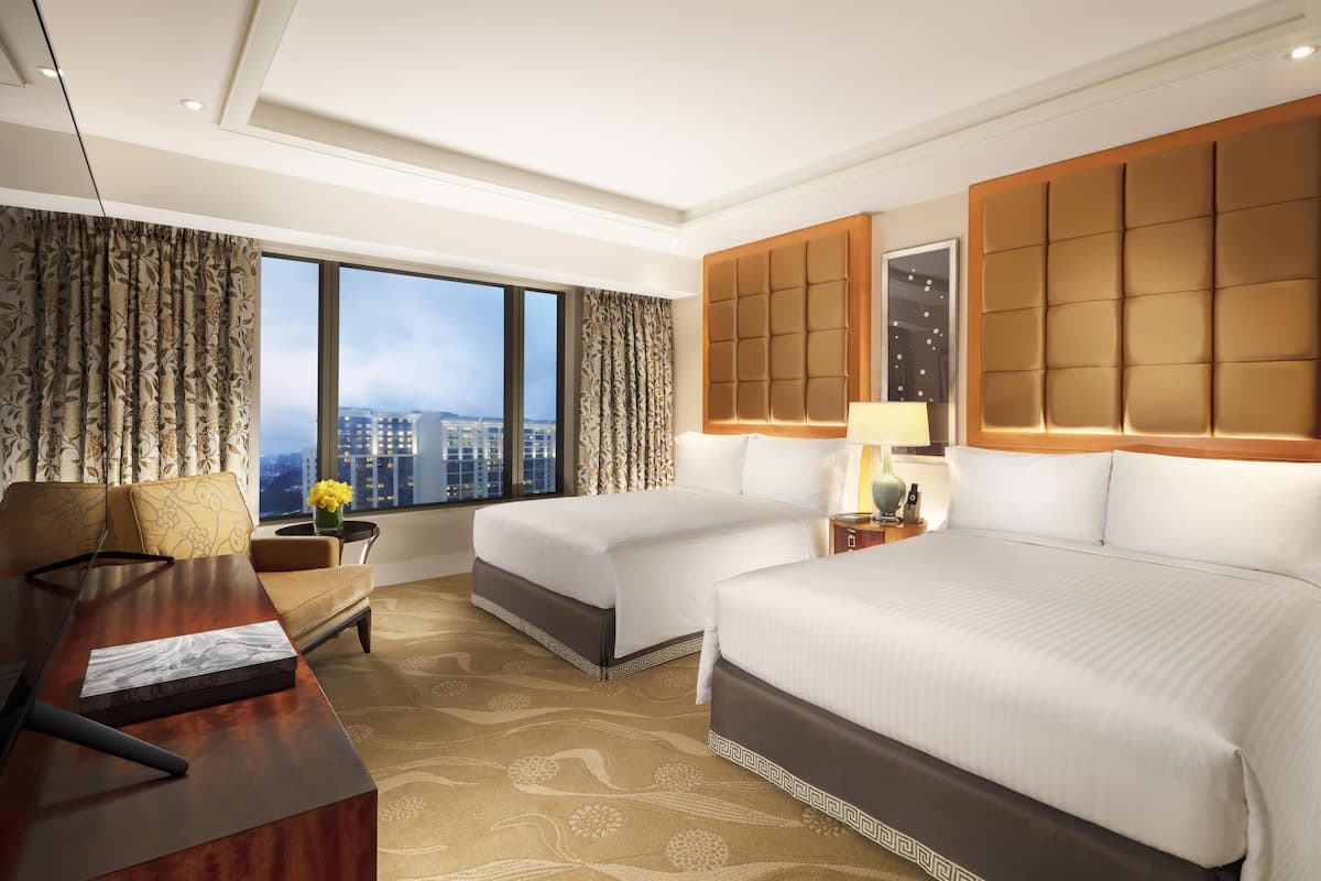 Habitación de hotel con dos camas, un escritorio, una silla, un ventanal con vista a edificios y una alfombra estampada.