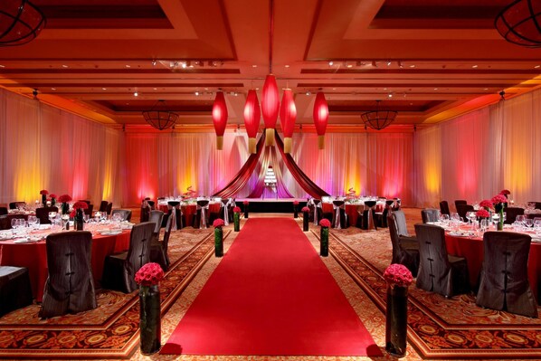 Un salón de banquetes con alfombra roja, mesas redondas y sillas dispuestas para un evento formal.
