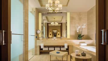 A modern bathroom with a large mirror, a chandelier, a bathtub, and a small table with a bowl and book.