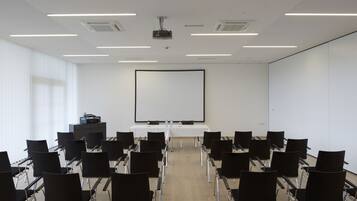 Ein Konferenzraum mit einer großen weißen Leinwand, Reihen schwarzer Stühle und einem an der Decke befestigten Projektor.