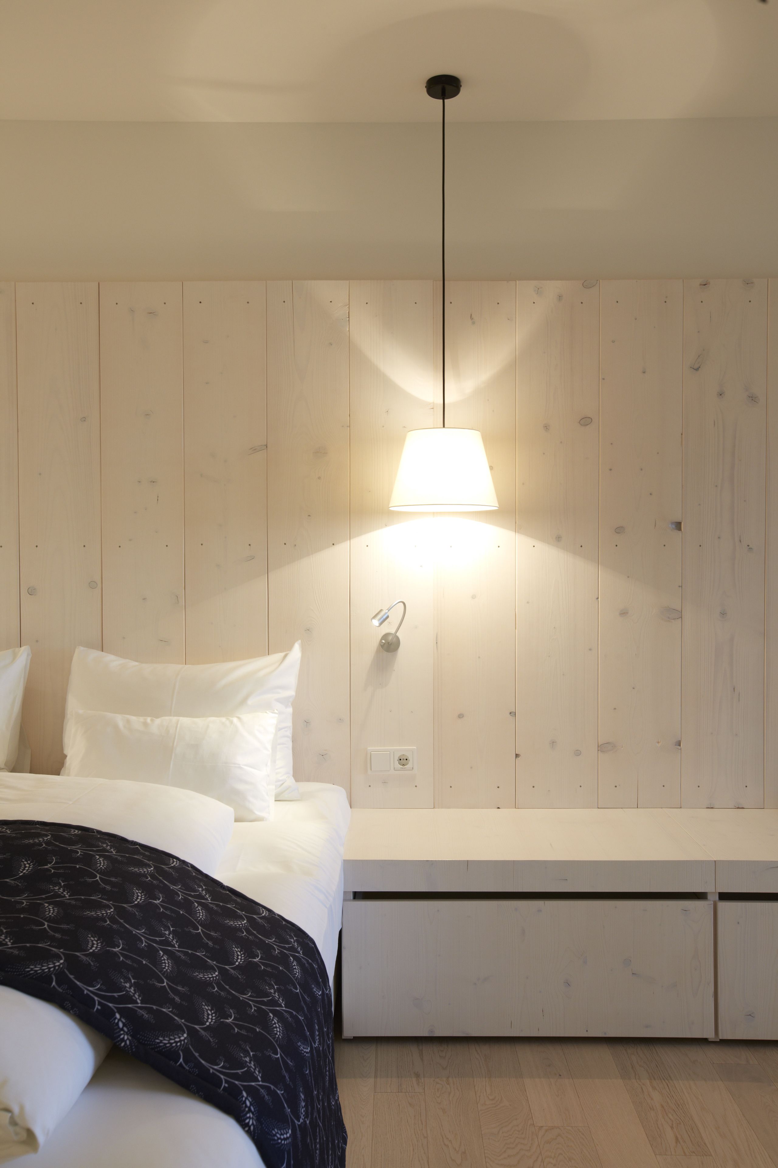 Un dormitorio con cama, mesita de noche y lámpara colgante.