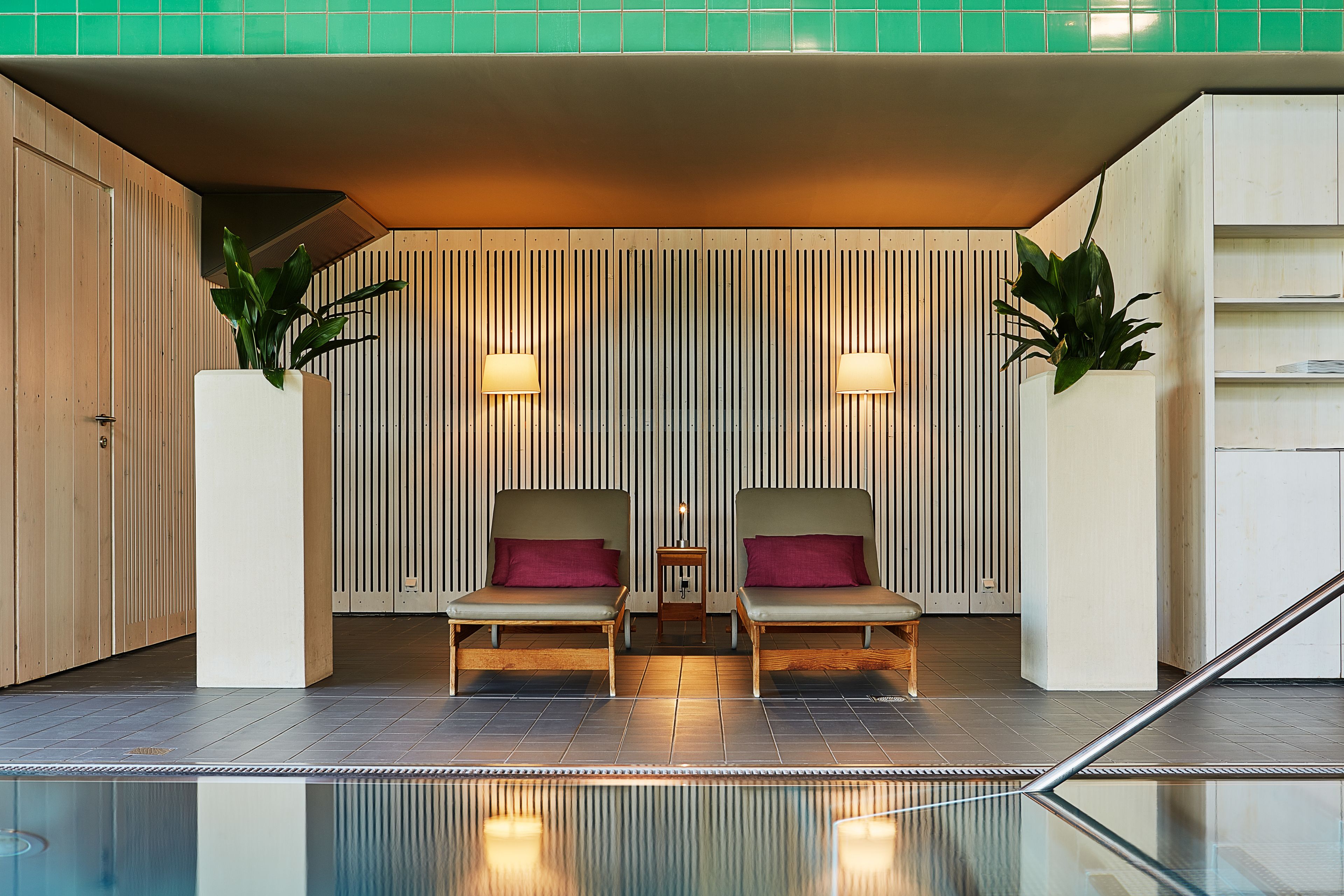 A modern lobby with two wooden chairs, a small table, and two potted plants.