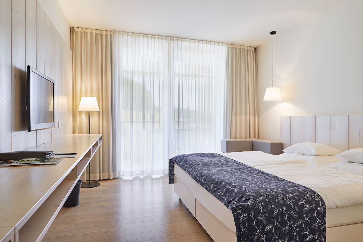 Ein Hotelzimmer mit Bett, Nachttisch, Lampe und Fernseher an einer Holzwand.