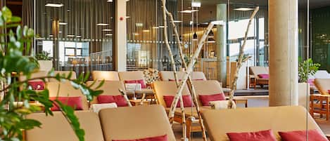 Vestíbulo de hotel con filas de sillones reclinables, un pilar grande y vista al interior a través de amplias ventanas.
