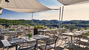 An outdoor dining area with tables and chairs, large umbrellas, and a scenic mountain view. - Loisium Wine & Spa Hotel Südsteiermark  (Ehrenhausen an der Weinstraße)
