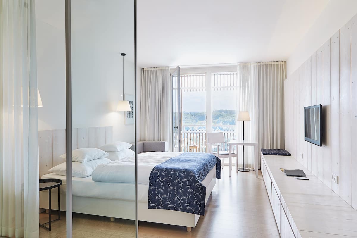 Ein modernes Hotelzimmer mit einem großen Bett, einem Schreibtisch, einem Fernseher und einem Balkon mit Blick.