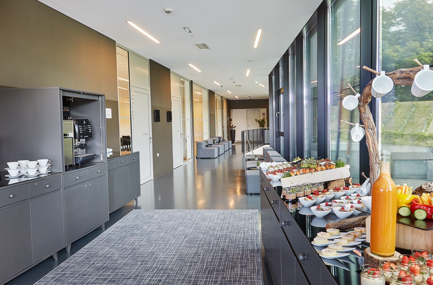 A modern kitchen area with a coffee machine, a buffet table with various food items, and a seating area with sofas and a coffee machine.