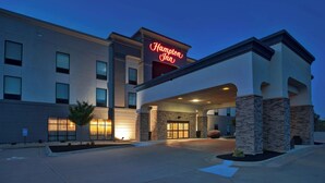 A Hampton Inn hotel with a modern facade, large windows, and a prominent neon sign. - Hampton Inn Clinton, IA (Clinton)